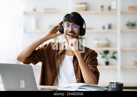Ragazzo indiano gioioso con cuffia seduta alla scrivania, canto karaoke Foto Stock