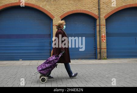 Una donna che indossa attrezzature personali protettive cammina con un carrello per lo shopping davanti a un negozio vicino a East Ham, nella zona est di Londra, mentre il Regno Unito continua a bloccarsi per contribuire a frenare la diffusione del coronavirus. Data foto: Martedì 28 aprile 2020. Foto Stock