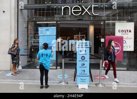 Un membro del personale aiuta gli acquirenti all'esterno del negozio Next a Oxford Street, Londra, in quanto i negozi non essenziali in Inghilterra aprono le loro porte ai clienti per la prima volta da quando le restrizioni di blocco del coronavirus sono state imposte a marzo. Data foto: Lunedì 15 giugno 2020. Foto Stock