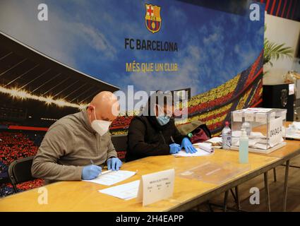 I funzionari che hanno indosso una maschera chirurgica e dei guanti attendono che gli elettori si esprimano allo stadio di calcio Camp Nou, che è stato trasformato in un seggio elettorale durante le elezioni regionali a Barcellona, in Catalogna, Spagna. Data foto: Domenica 14 febbraio 2021. Il credito fotografico dovrebbe essere: Isabel Infantes Foto Stock