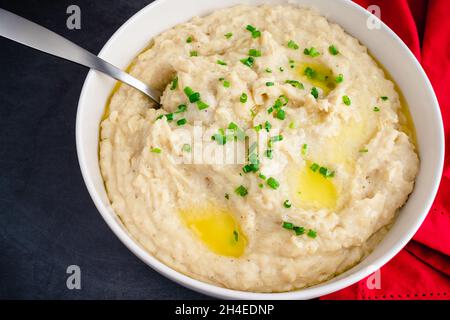 Purè di patate all'aglio in una ciotola da portata: Una grande ciotola di patate montate ricoperte di erba cipollina e burro fuso Foto Stock