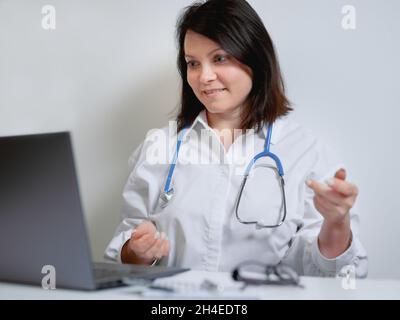 il medico femminile consulta il paziente in video chat. il medico femminile parla dal vivo guardando e parlando al computer portatile lavoro in clinica online per aiutare il paziente su Foto Stock