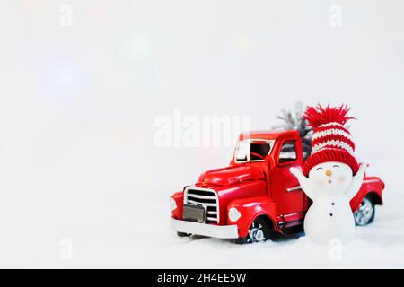 Snowman in un cappello rosso vicino rosso ritiro camion di natale, su uno sfondo bianco. Ritiro di natale buon natale e felice anno nuovo biglietto di auguri. Copia s. Foto Stock