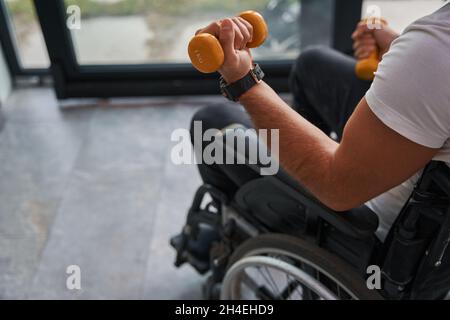 Uomo con disabilità fisica utilizzando una sedia a rotelle che tiene in mano attrezzature sportive Foto Stock
