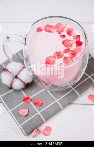 Matcha rosa con petali di rosa su sfondo bianco. Tazza trasparente con tè alla moda montato vegan. Latte lunare. Bevanda rilassante per il sonno. Foto Stock