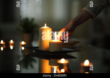 Primo piano delle candele di illuminazione della mano della donna nella notte scura a casa Foto Stock