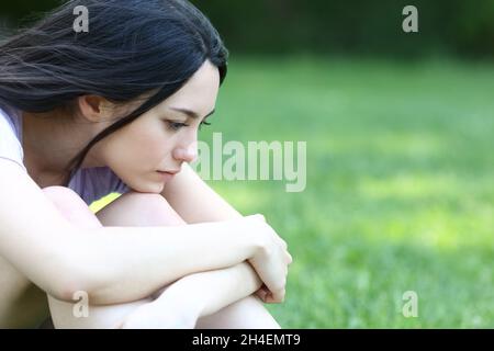 Triste donna asiatica che lamenta di essere seduta da sola in un parco Foto Stock