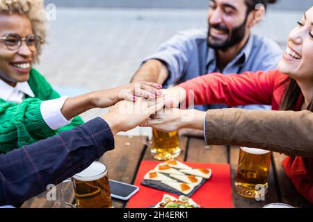 Gruppo multirazziale Unito di giovani studenti che si accatastano le mani al bar della birreria Foto Stock