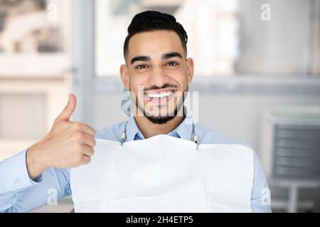 Servizi dentistici. Happy Arab Guy seduto in sedia dentista, mostrando Thumb Up Foto Stock