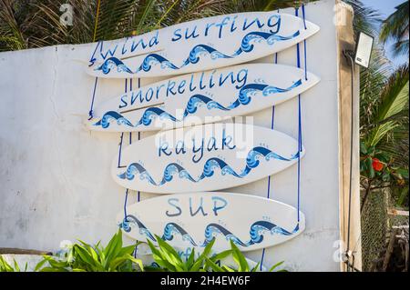 Tavole da surf decorative con diversi tipi di sport acquatici scritti su ciascuno, Diani, Kenya Foto Stock