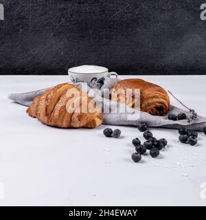 Croissant e dolce farcito di cioccolato, con bacche fresche e tazza di caffè con crema su sfondo marmoreo. Foto Stock