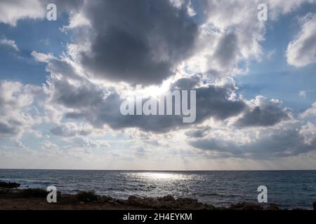 Alberi di luce del sole si infrangono attraverso le nuvole sopra Coral Bay, Paphos, Cipro. Foto Stock