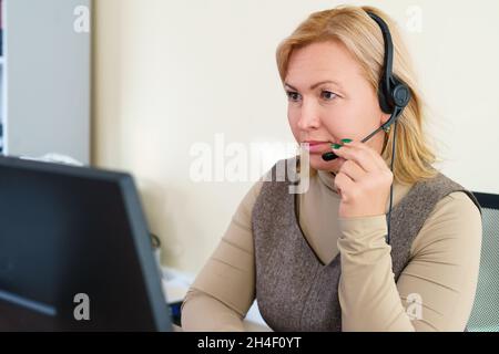 Un bel dipendente del call center ascolta attentamente e regola le cuffie. Business o lavoro da casa concetto. Foto Stock