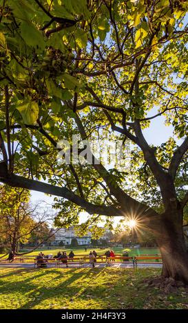 Wien, Vienna: park Stadtpark, le persone alle panchine godono l'ultimo sole della giornata, colori autunnali, vista al Kursalon Hübner nel 01. Città vecchia, Vienna, Austria Foto Stock