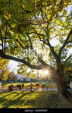 Wien, Vienna: park Stadtpark, le persone alle panchine godono l'ultimo sole della giornata, colori autunnali, vista al Kursalon Hübner nel 01. Città vecchia, Vienna, Austria Foto Stock