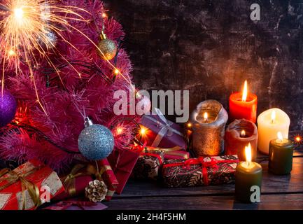 Atmosfera di Natale o di Capodanno composizione, un piccolo albero rosa di natale su sfondo nero, coni, una candela bruciante, regali e albero di Natale de Foto Stock