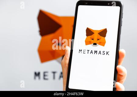 Ucraina, Odessa - Ottobre, 9 2021: Tenere la mano mobile con l'app MetaMask in esecuzione sullo schermo dello smartphone con il logo MetaMask sullo sfondo. MetaMask è così Foto Stock