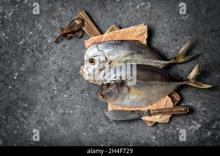 Vista dall'alto del gustoso vasetto di pesce di mare secco salato o di Selena con coltello in argento su tagliere in legno e fondo in cemento grigio Foto Stock