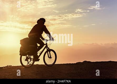 Il motociclista in mountain bike con zaino viaggia sullo sfondo dell'alba Foto Stock