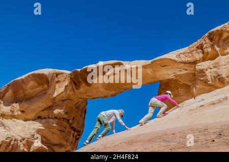 WADI RUM, GIORDANIA - 26 MARZO 2017: I turisti che si arrampicano sul ponte di roccia di Burdah nel deserto di Wadi Rum, Giordania Foto Stock