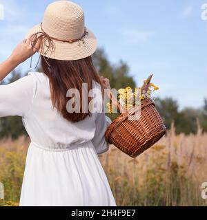 Donna che spezza un cesto di fiori selvatici. Donna che raccoglie fiori / erbe in natura. Foto Stock