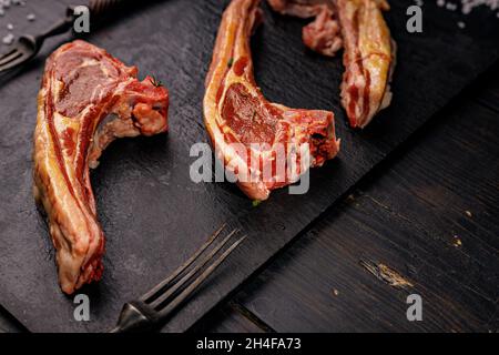 Primo piano costolette di agnello crudo. Carne halal. Carne cruda. Rack di agnello su sfondo rustico scuro. Sale e spezie. Halal cibo ancora vita. Spazio di copia Foto Stock