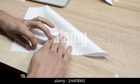 Primo piano della carta originale pieghevole. Riprese in stock. Le mani degli uomini sono piegate da carta bianca origami o aeroplano. Classe Origami durante la pausa al lavoro. Foto Stock