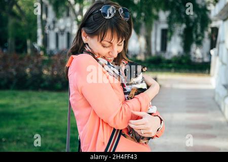 Felice giovane donna caucasica che abbraccia il suo cane piccolo, russo Toy o russo Toy Terrier, vestito in tuta d'autunno. Concetto di amore per gli animali domestici Foto Stock