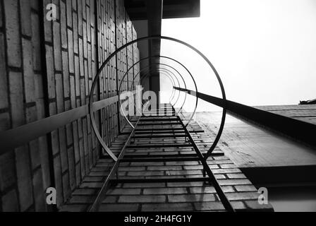 Scatto in scala di grigi ad angolo basso di una scala in metallo su un edificio in pietra Foto Stock