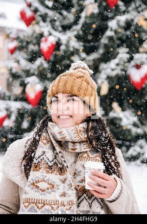 Ritratto di una giovane donna che indossa eleganti abiti invernali in città innevata, bevendo un caffè da portare via Foto Stock