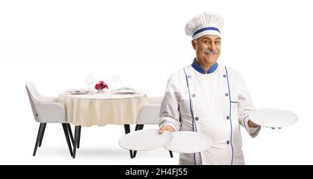 Chef allegro e maturo sorridendo e tenendo tre piatti di fronte ad un tavolo da ristorante isolato su sfondo bianco Foto Stock