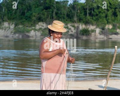 Amazzonia. America Latina - Sep 2017: Ritratto di una donna felice in un cappello, un abitante locale della foresta pluviale amazzonica - una rete di pesca in disfacimento su un sa Foto Stock