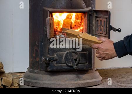 Uomo che mette il ceppo a legna bruciando stufa Foto Stock