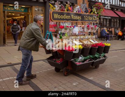 Un venditore di strada che spinge un barrow di fiori, rose di legno, e biscotti lungo la strada. Foto Stock