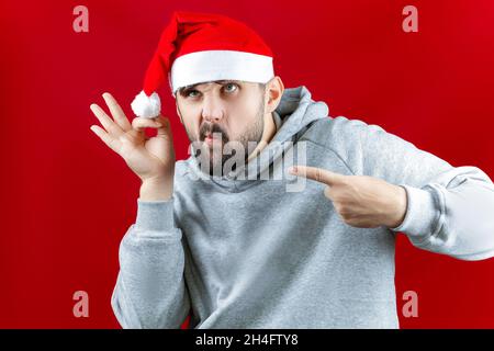 Un uomo vestito di Natale mostra un segno OK e punta ad esso con il suo indice dito Foto Stock