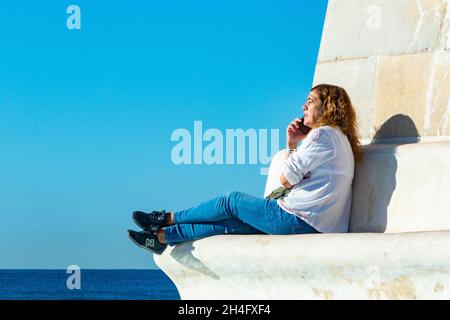 Donna su cellulare seduto sul monumento in pietra sul lungomare di Palma Mallorca Foto Stock