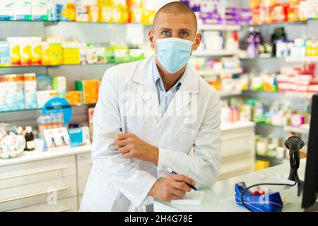 Ritratto del farmacista in maschera medica lavorando al registratore di cassa in farmacia Foto Stock