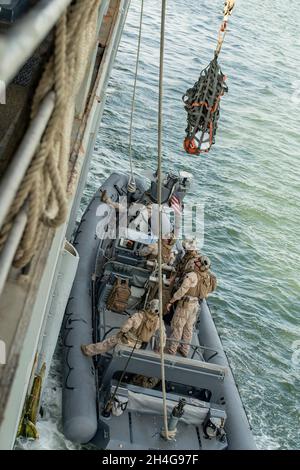 211026-M-ON629-1009 ATTIVITÀ DI SUPPORTO NAVALE BAHRAIN (OTT 26, 2021) Marines assegnato alla squadra di barca di distacco di tutti i domini di ricognizione, 11th Marine Expeditionary Unit (MEU), trasferire il contrabbando simulato ai marinai a bordo della nave di sbarco anfibio USS Pearl Harbor (LSD 52) durante un esercizio di recupero di contrabbando presso Naval Support Activity Bahrain, ottobre 26. Pearl Harbor e l'11° MEU sono dislocati nella 5th Fleet area degli Stati Uniti di operazioni a sostegno delle operazioni navali per garantire la stabilità e la sicurezza marittima nella regione centrale, collegando il Mediterraneo e il Pacifico attraverso il W Foto Stock