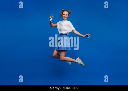 felicità, libertà, movimento e concetto di persone - sorridente giovane donna che salta in aria su sfondo blu, Foto Stock