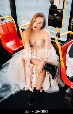 Una sposa in un abito da sposa con lunghe passeggiate per capelli nel trasporto della città di Breslavia. Modello sposa seduto su un sedile di autobus, Polonia. Foto Stock