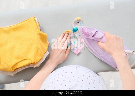 Giovane donna incinta che stira calzini a casa Foto Stock