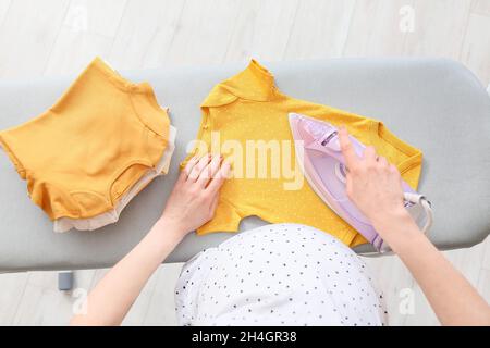 Giovane donna incinta che stira il bodysuit del bambino a casa Foto Stock