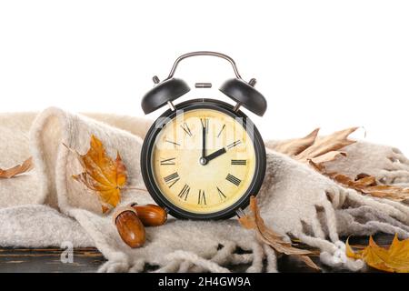 Sveglia, ghiande, sciarpa e foglie d'autunno su tavola su sfondo bianco. Fine ora legale Foto Stock