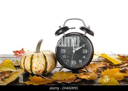 Sveglia, zucca e foglie d'autunno sul tavolo su sfondo bianco Foto Stock