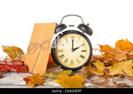 Sveglia, busta e foglie d'autunno sul tavolo su sfondo bianco. Fine ora legale Foto Stock