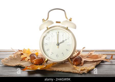 Sveglia, ghiande e foglie d'autunno su tavola su sfondo bianco. Fine ora legale Foto Stock