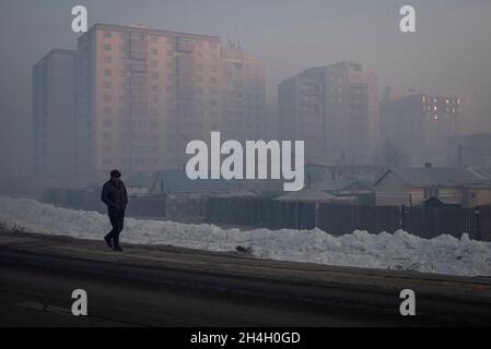 Un uomo cammina oltre i blocchi di appartamento città durante una mattinata molto inquinata in Ulaanbaatar, Mongolia, 19 gennaio 2019. Durante il duro inverno mongolo Foto Stock