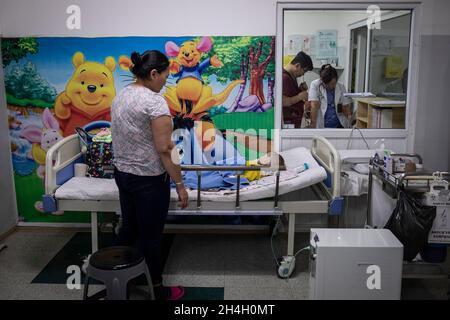 Una madre guarda il bambino che soffre di complicazioni respiratorie in un'unità di emergenza pediatrica in uno degli ospedali cittadini della capitale Foto Stock