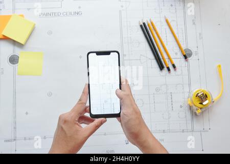 Mani di ingegnere civile scattando foto del piano di costruzione su smartphone, vista dall'alto Foto Stock