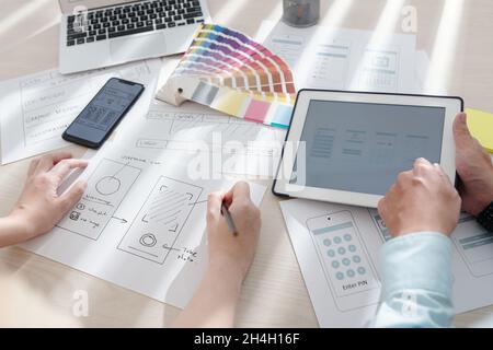 Progettisti UI e UX che lavorano alla progettazione di applicazioni mobili, disegnando schizzi e scegliendo la tavolozza dei colori Foto Stock